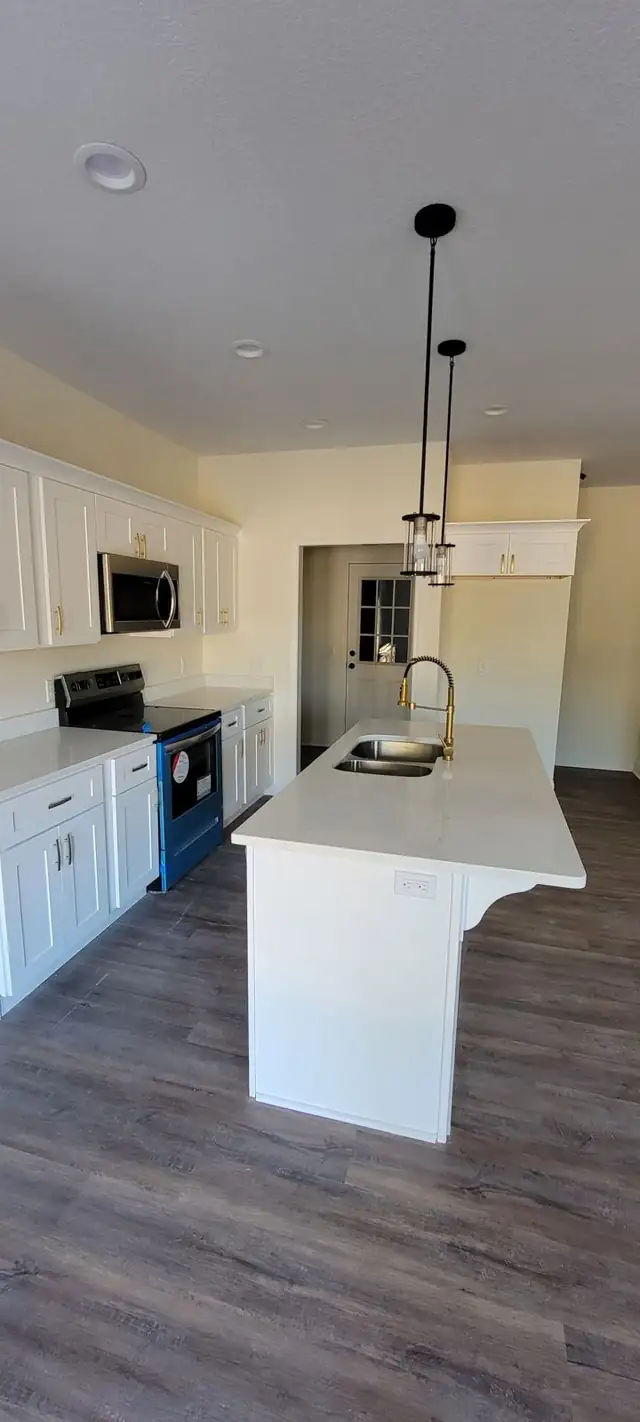 White kitchen with a white countertop island, undermount sink, gold faucet and pendant lights