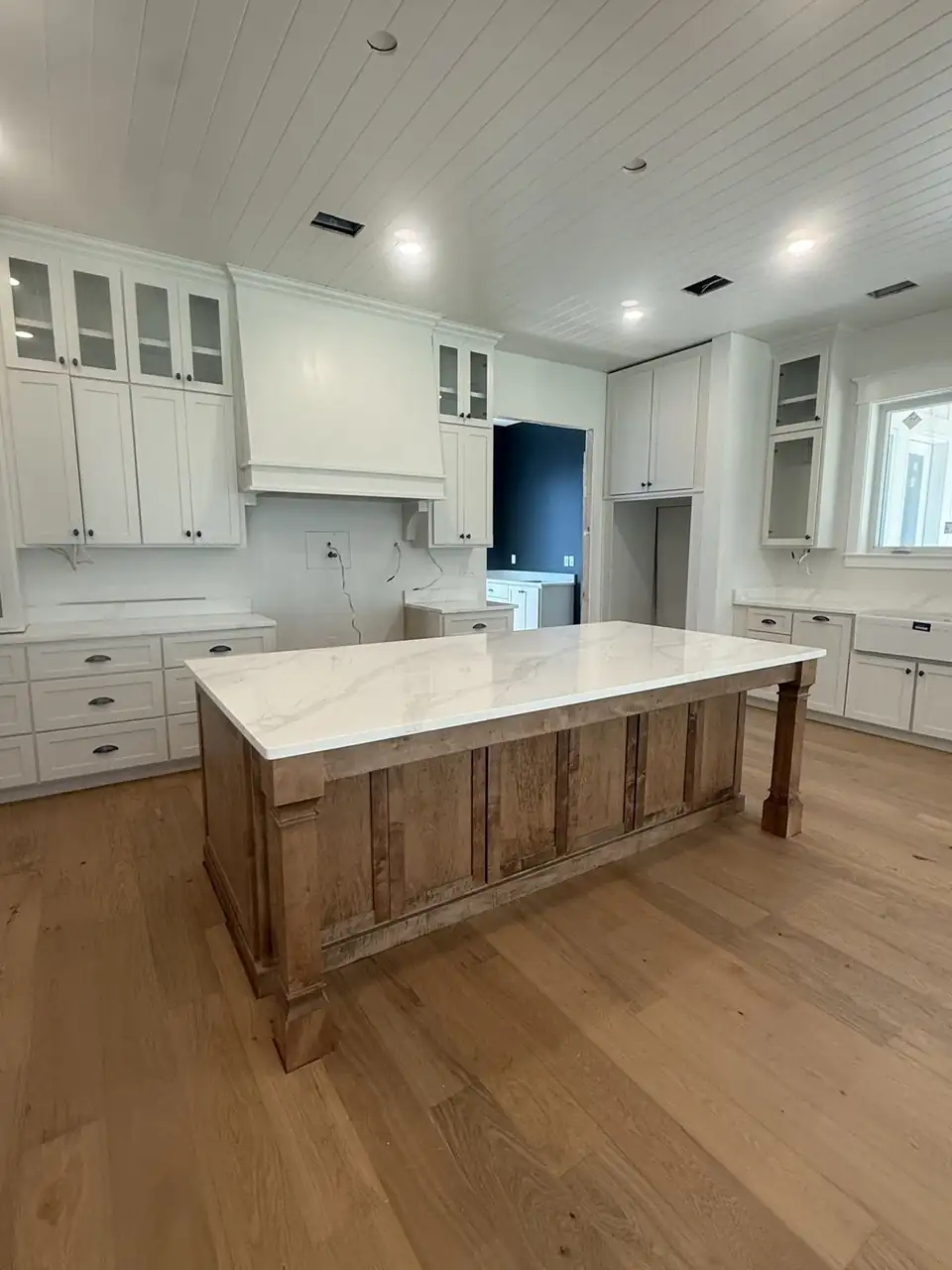 Countertop by Solid Surfaces, a granite countertops fabricator in Jesup, GA: white veined top on a stained wood island with white shaker cabinets and a plank ceiling