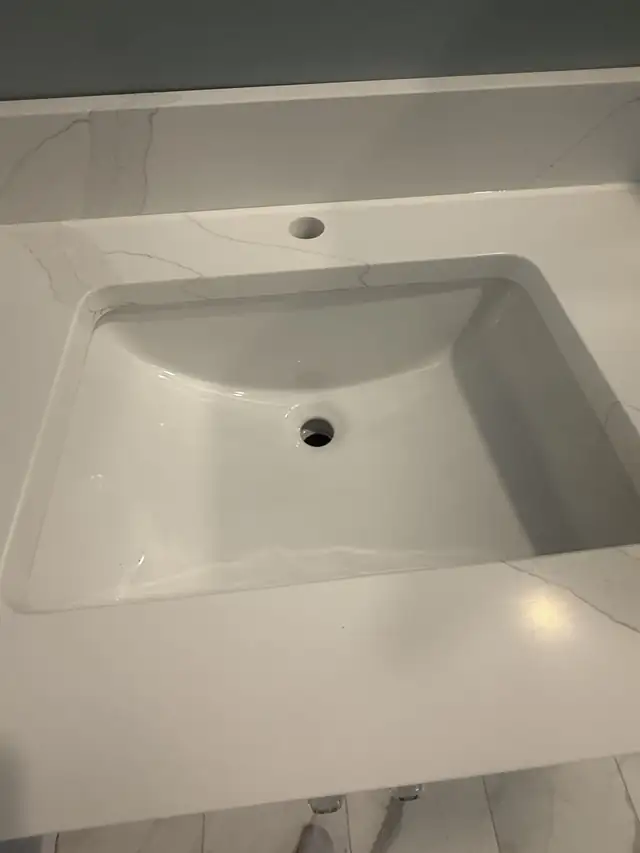 Close-up of a white undermount sink set into a white veined countertop with a faucet hole