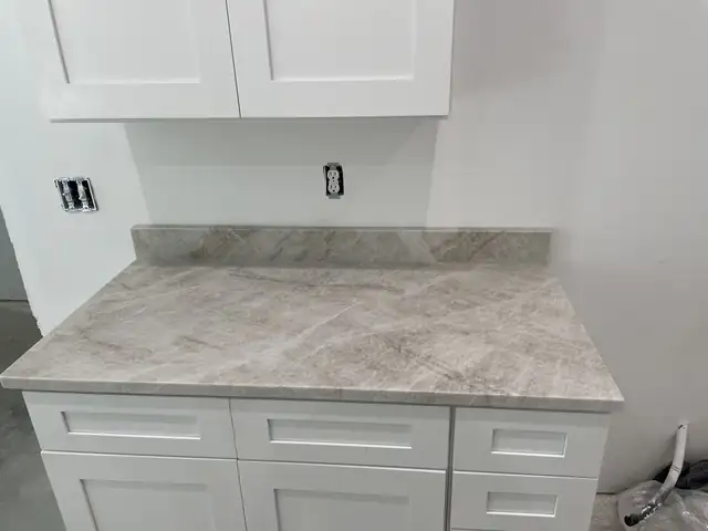 Gray and white veined stone countertop with matching backsplash on white shaker base cabinets