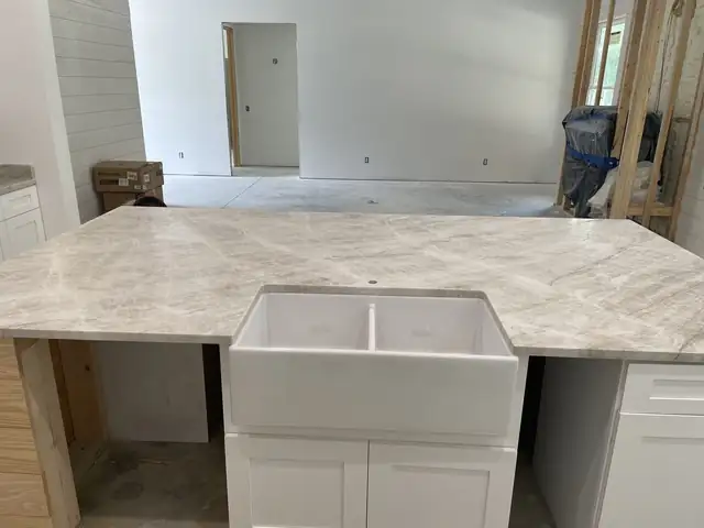 Taupe and white stone countertop over a white farmhouse sink on a new kitchen island