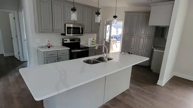 White countertop with gray veining on a large island with an undermount stainless sink and gray cabinets