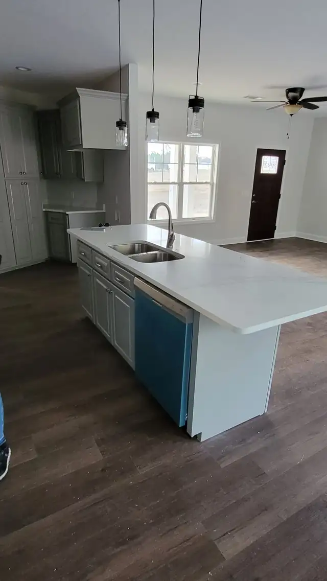 New-construction kitchen with a white veined island top, gray cabinets and a dishwasher still in blue protective film